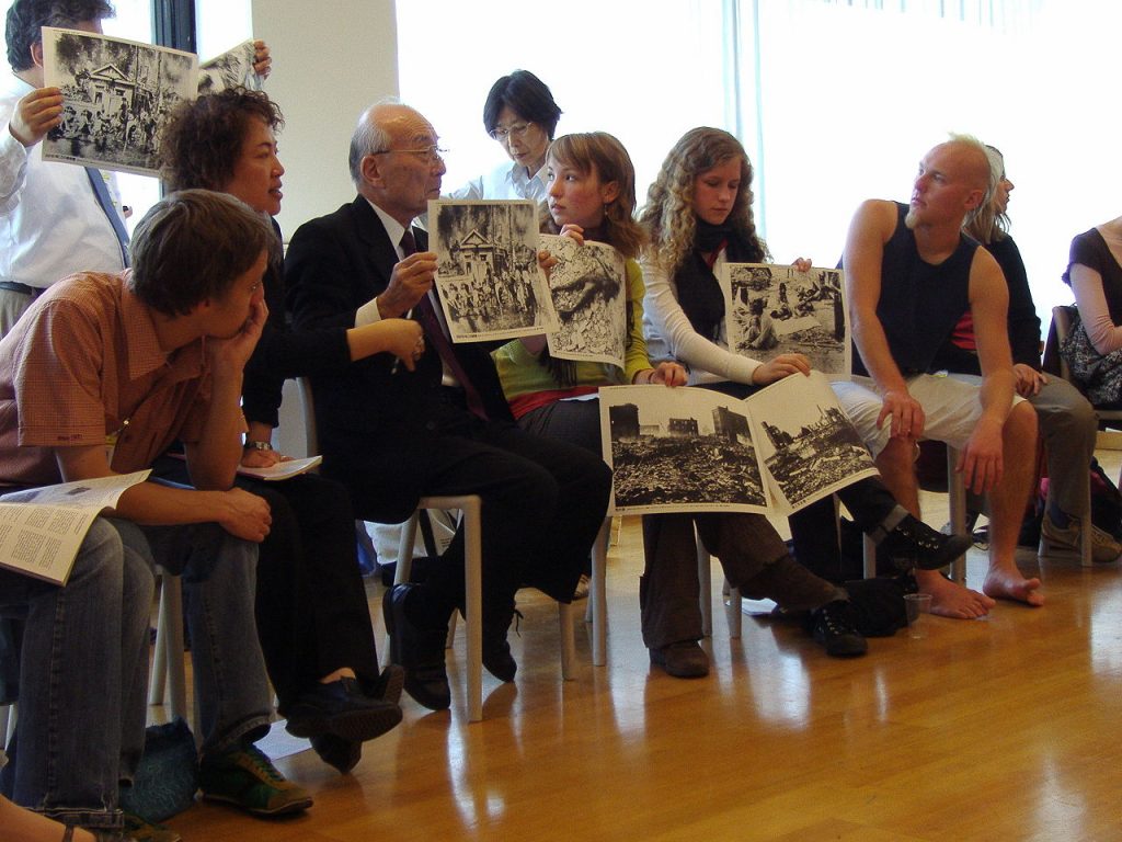 A hibakusha, a survivor of the atomic bombing of Nagasaki, tells young people about his experience and shows pictures. United Nations building in Vienna, duringt the NPT PrepCom 2007. By Buroll (Own work) [Public domain], via Wikimedia Commons